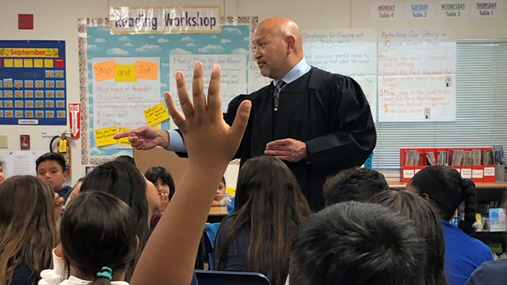 judge in robe in classroom and student's hand raised