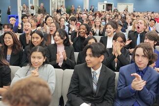 students in suits seated and clapping in assembly