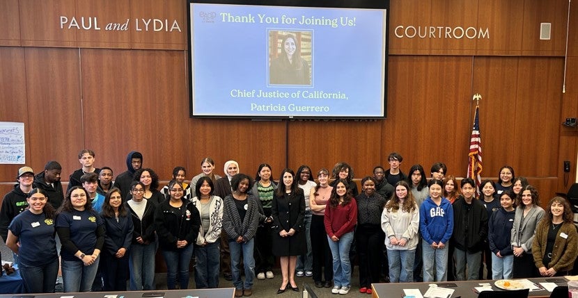 students stand with chief justice inside wood paneled mock courtroom