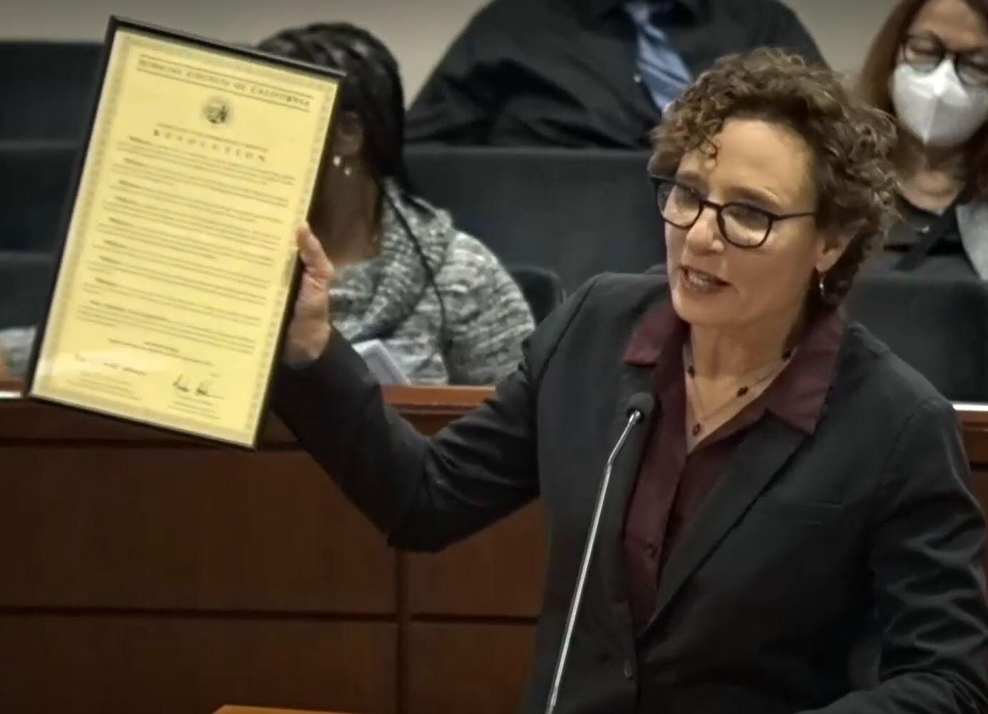 woman holding up resolution behind podium in boardoom