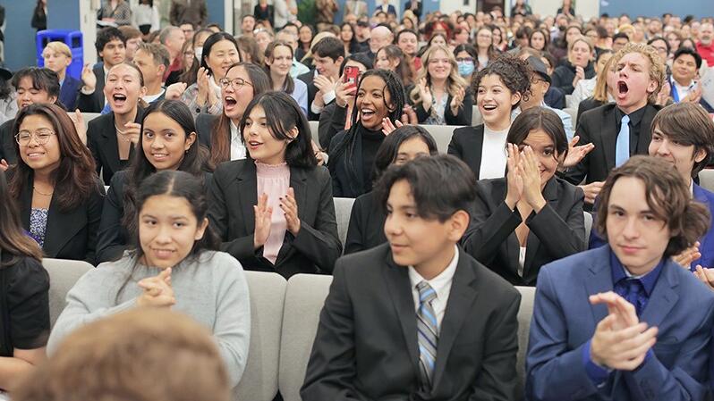 students in suits seated and clapping in assembly