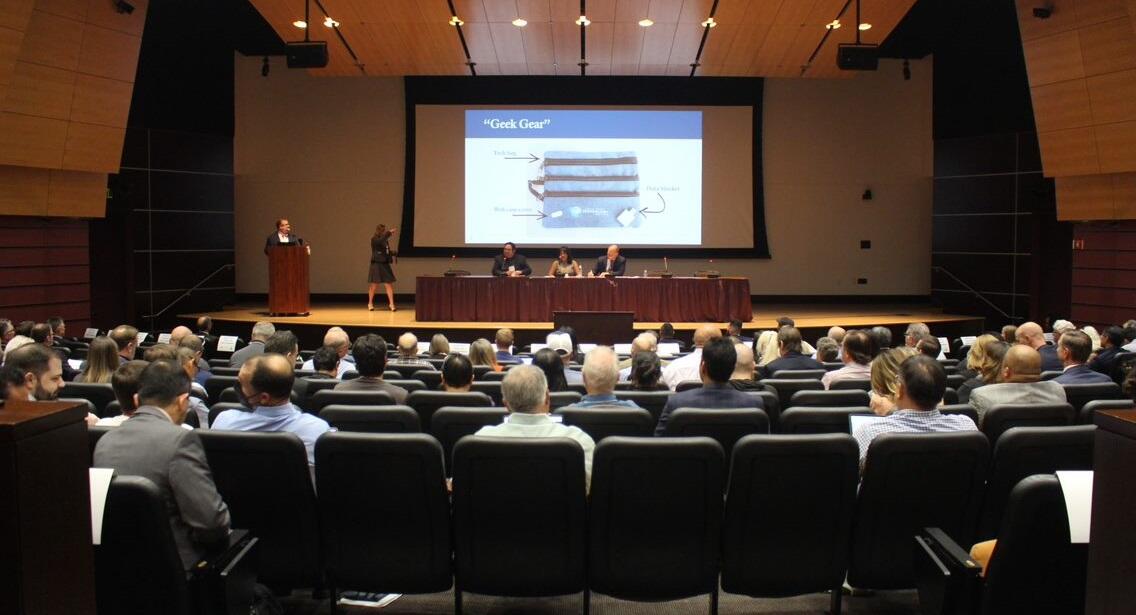 Auditorium filled with attendees and panelists seated on stage 