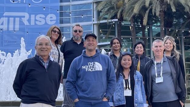 men and women stand in front of We are AllRise banner outside