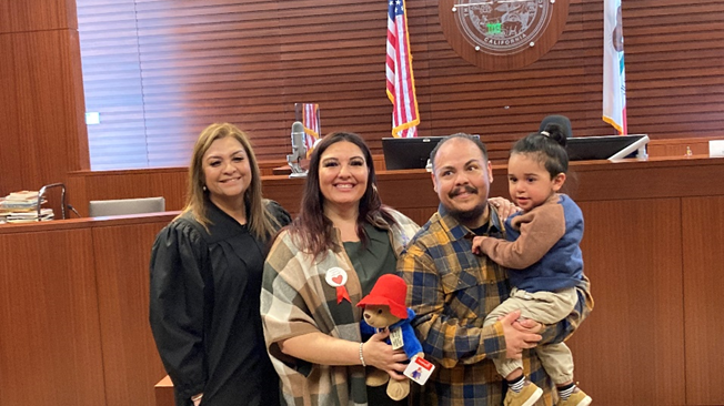 A judge and a family of 3 standing in the middle of a courtroom after adoption hearing