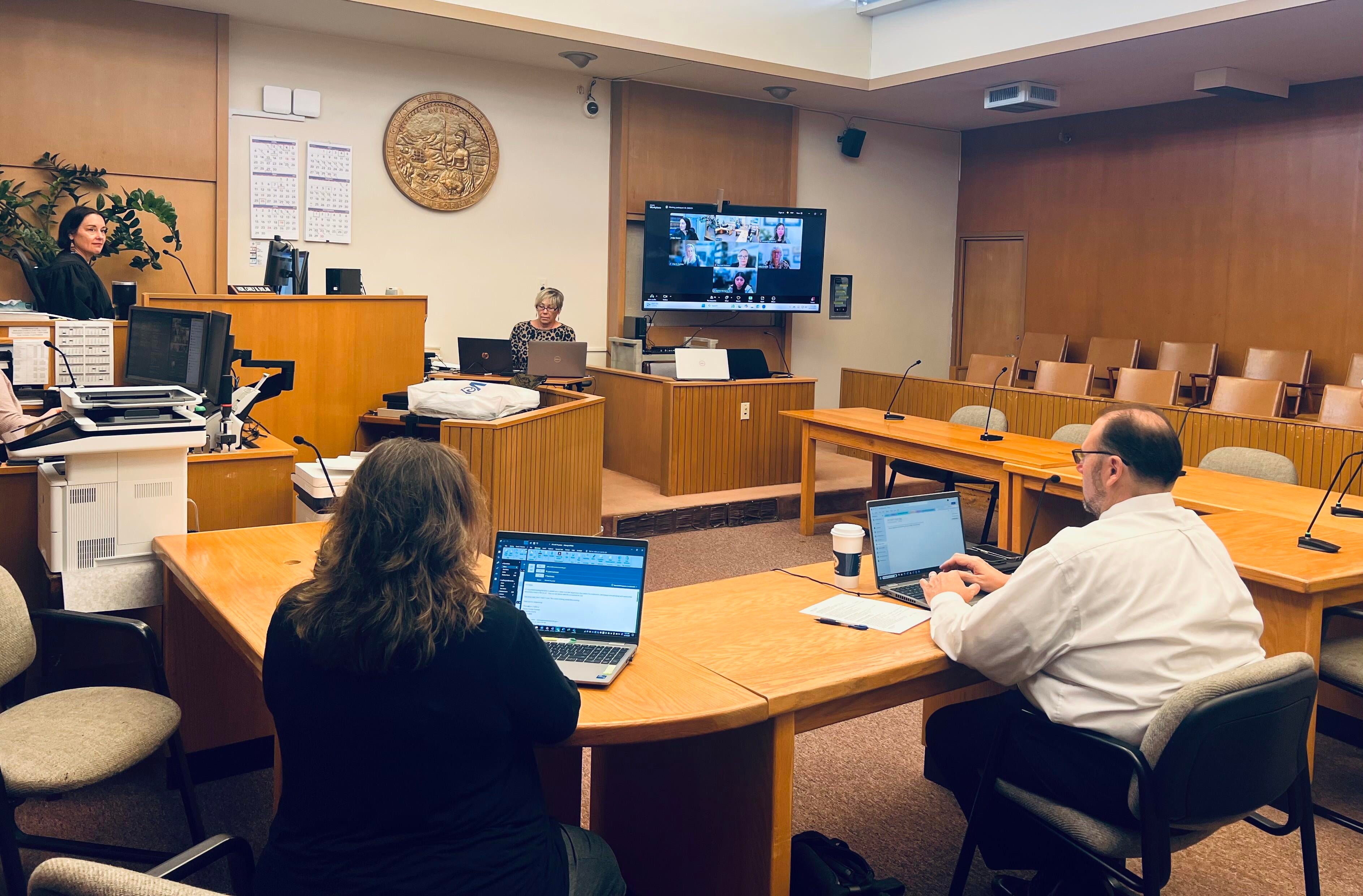 A remote proceeding that took place in the Mendocino Superior Court. A female judge sitting on the left side of the courtroom, and a screen showing remote participants is on the right side of the room.