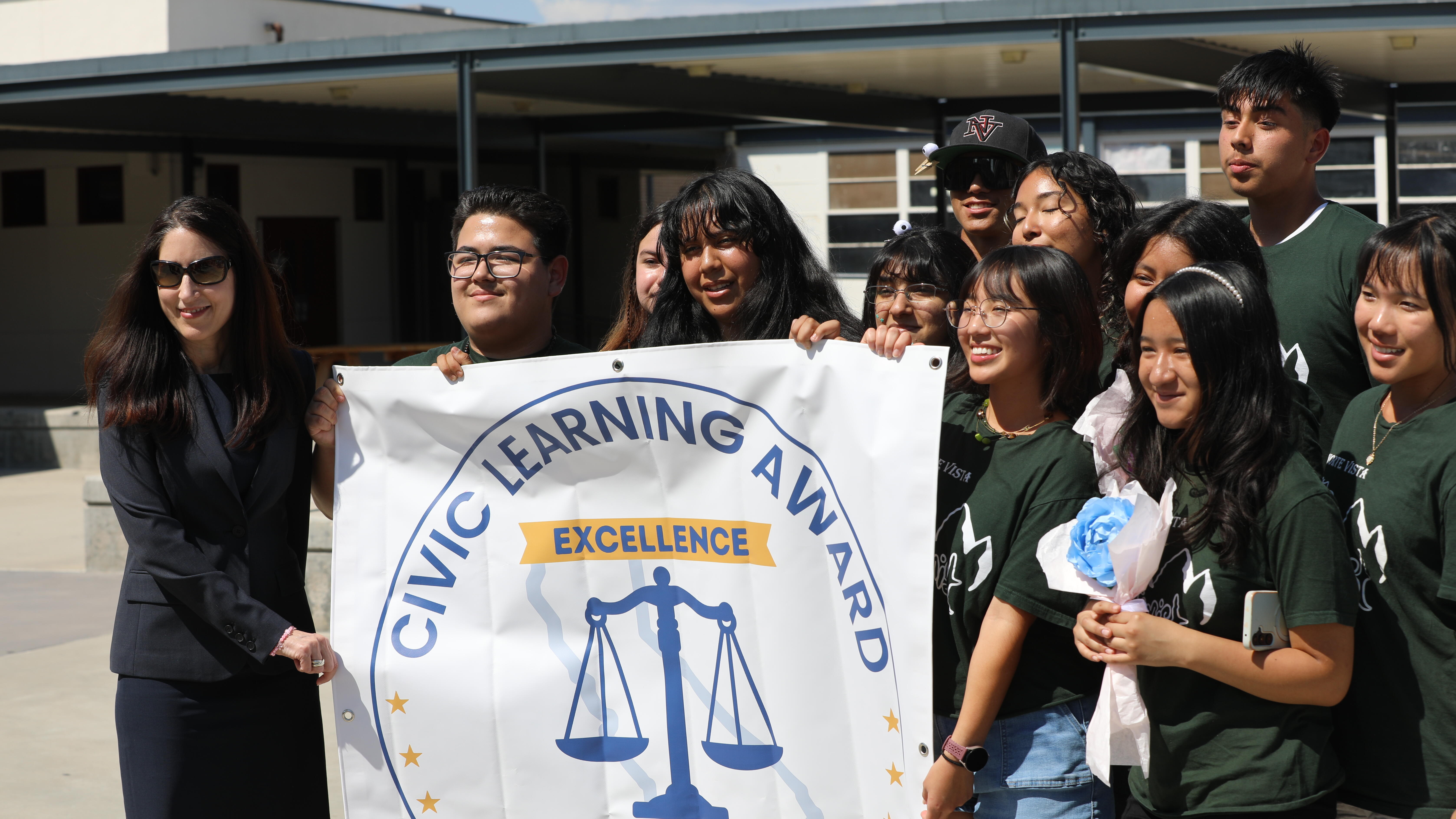 Chief Justice Patricia Guerrero stands next to a group of students holding a sign designating them as Civic Learning Award of Excellence recipients.