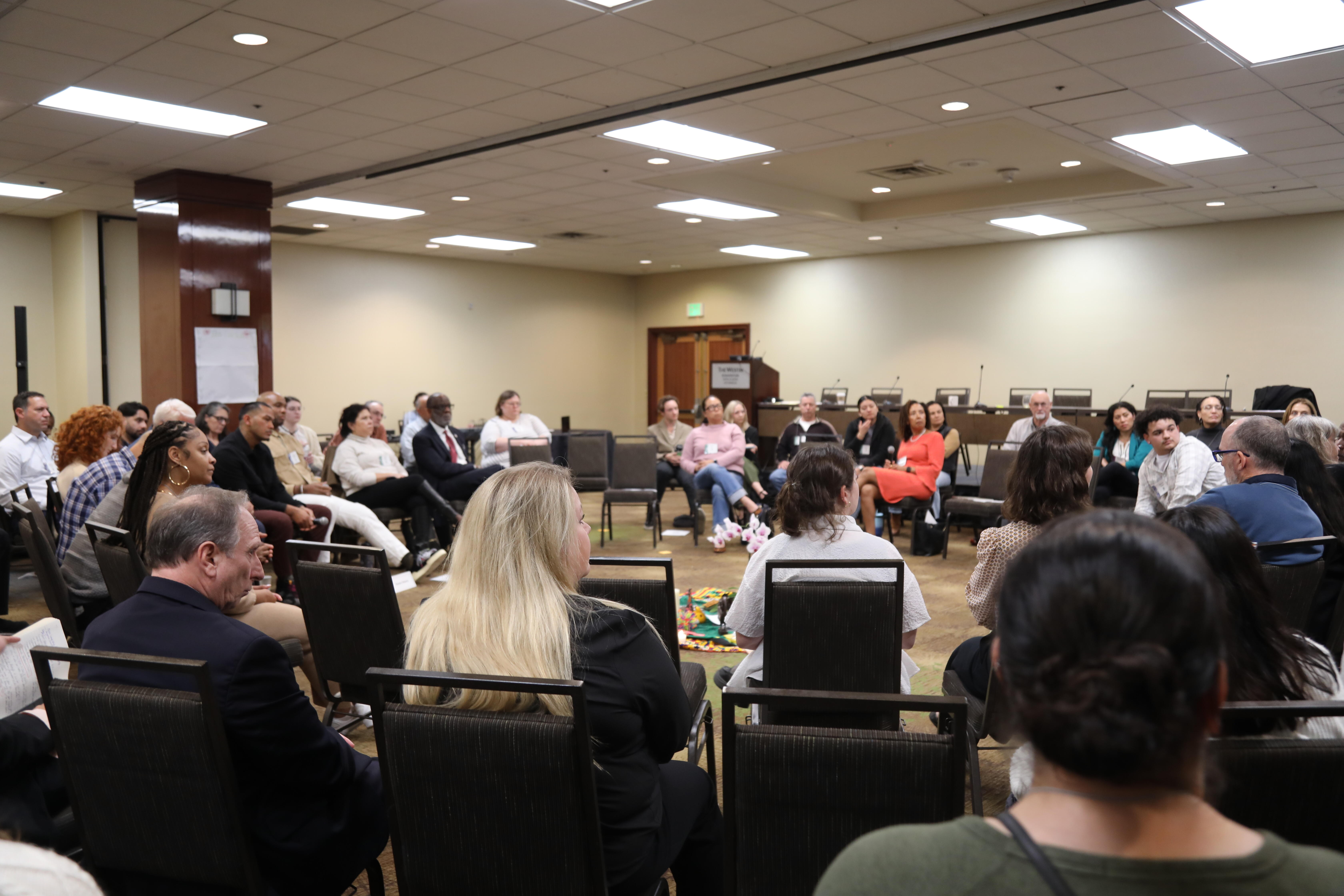 Attendees sit in conference room in circle