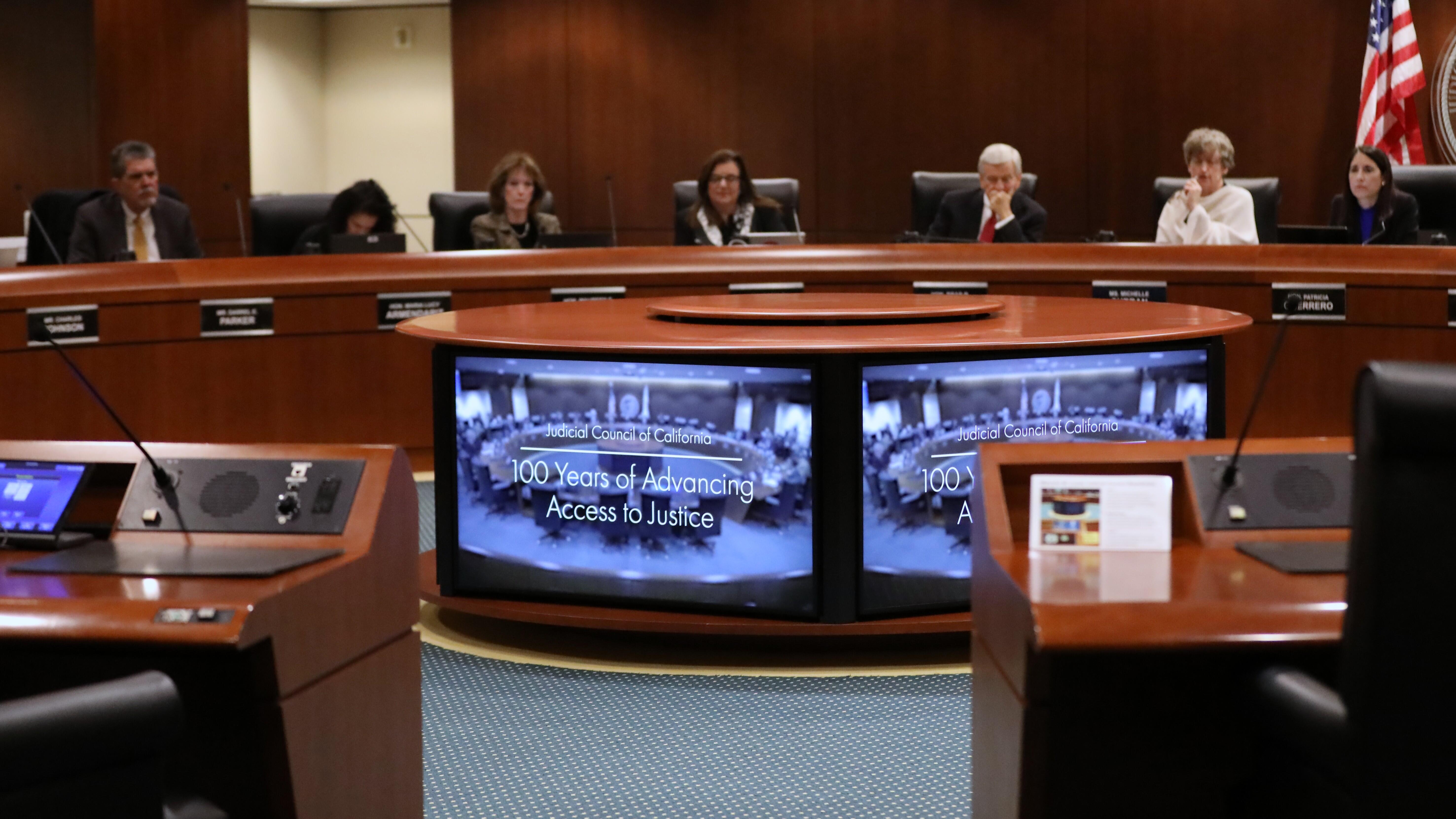 People sitting around a boardroom table looking at a monitor displaying the words "100 Years of Advancing Access to Justice"