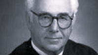 Man with glasses in judicial attire.