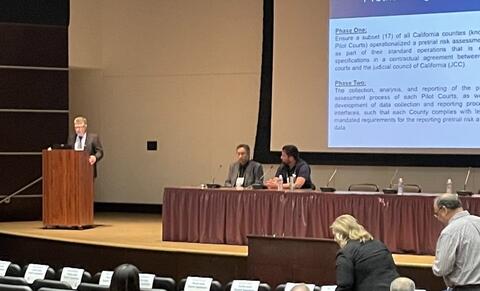 Presenters on stage with large screen behind them