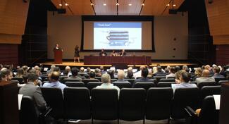 Auditorium filled with attendees and panelists seated on stage