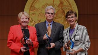 Three people standing next to each other, each holding an award