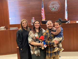 A judge and a family of 3 standing in the middle of a courtroom after adoption hearing