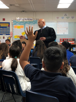 judge in robe in classroom and student's hand raised