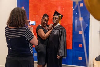 Person taking a photo of two people, one wearing a graduate cap and gown