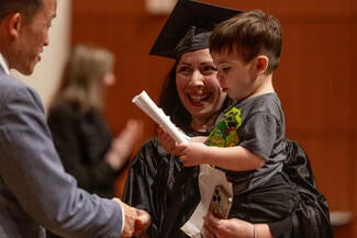Person shaking hands with another person holding a small boy that is holding a diploma