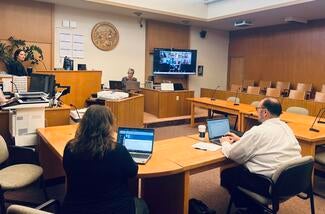A remote proceeding that took place in the Mendocino Superior Court. A female judge sitting on the left side of the courtroom, and a screen showing remote participants is on the right side of the room.