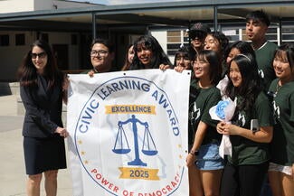 Chief Justice Patricia Guerrero stands next to a group of students holding a sign designating them as Civic Learning Award of Excellence recipients.