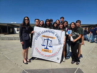 Chief Justice Patricia Guerrero stands next to a group of students holding a sign designating them as Civic Learning Award of Excellence recipients.