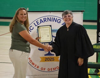 Judge with glasses shakes hand with a teacher holding a framed award.