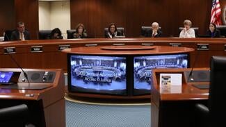 People sitting around a boardroom table looking at a monitor displaying the words "100 Years of Advancing Access to Justice"
