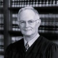 Justice Daniel J Kremer in judicial attire in front of bookshelf.