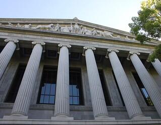 Facade of building with white columns and sculpted figures in a triangular frieze at the top.
