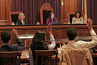 Judicial officers sit in chairs facing a row of students raising hands