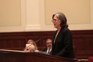 Justice Cody speaks at a wooden podium. 